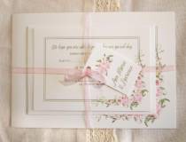 A floral wedding invitation set with a pink rose design all tied together with a pink ribbon and a tag with the bride and grooms names